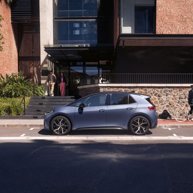 Modrý VW ID.3 Neo parkuje pred obytným domom, z ktorého vychádza žena a muž