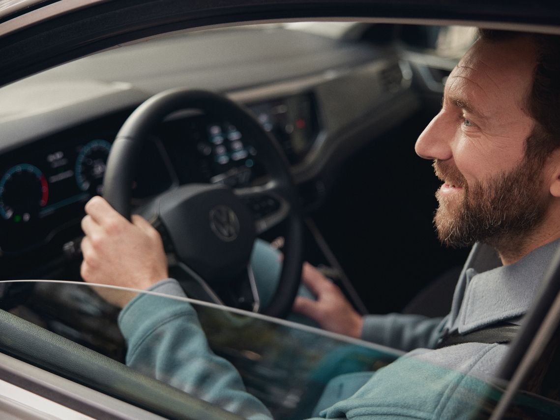 Muž sedí za volantom vozidla VW. Pohľad do interiéru cez čiastočne stiahnuté okno. 