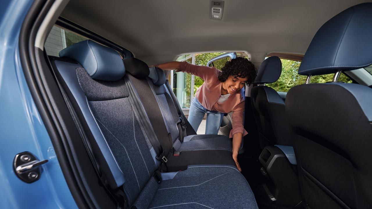 Mladá žena sklápá zadné sedadlo modrého VW T-Cross.