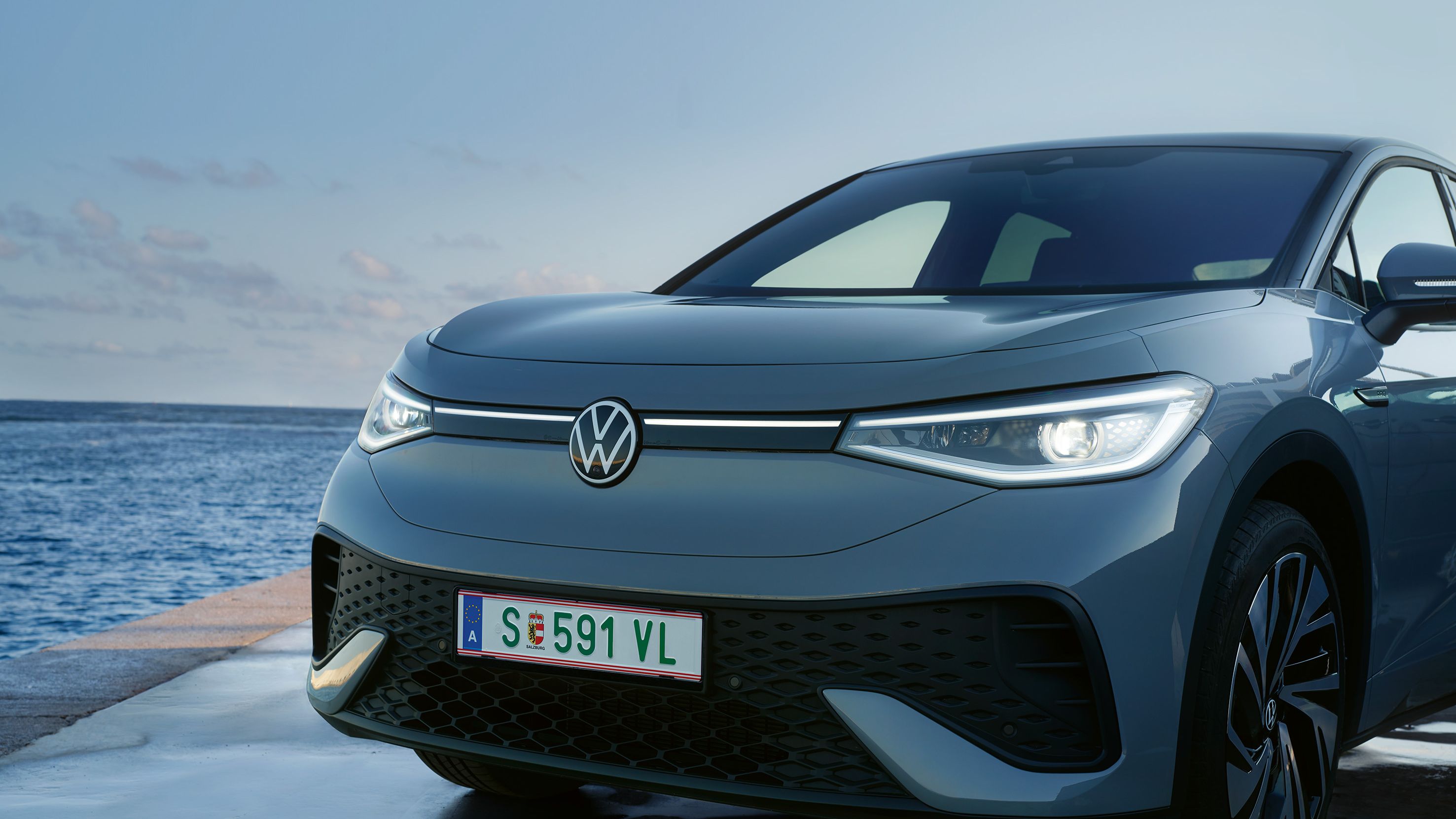 Volkswagen ID.5 zaparkovaný na móle pri mori. Auto má moderný dizajn s úzkymi prednými svetlami.