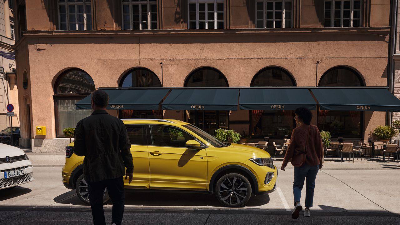 Muž a žena sa blížia k žltému VW T-Cross na okraji cesty.