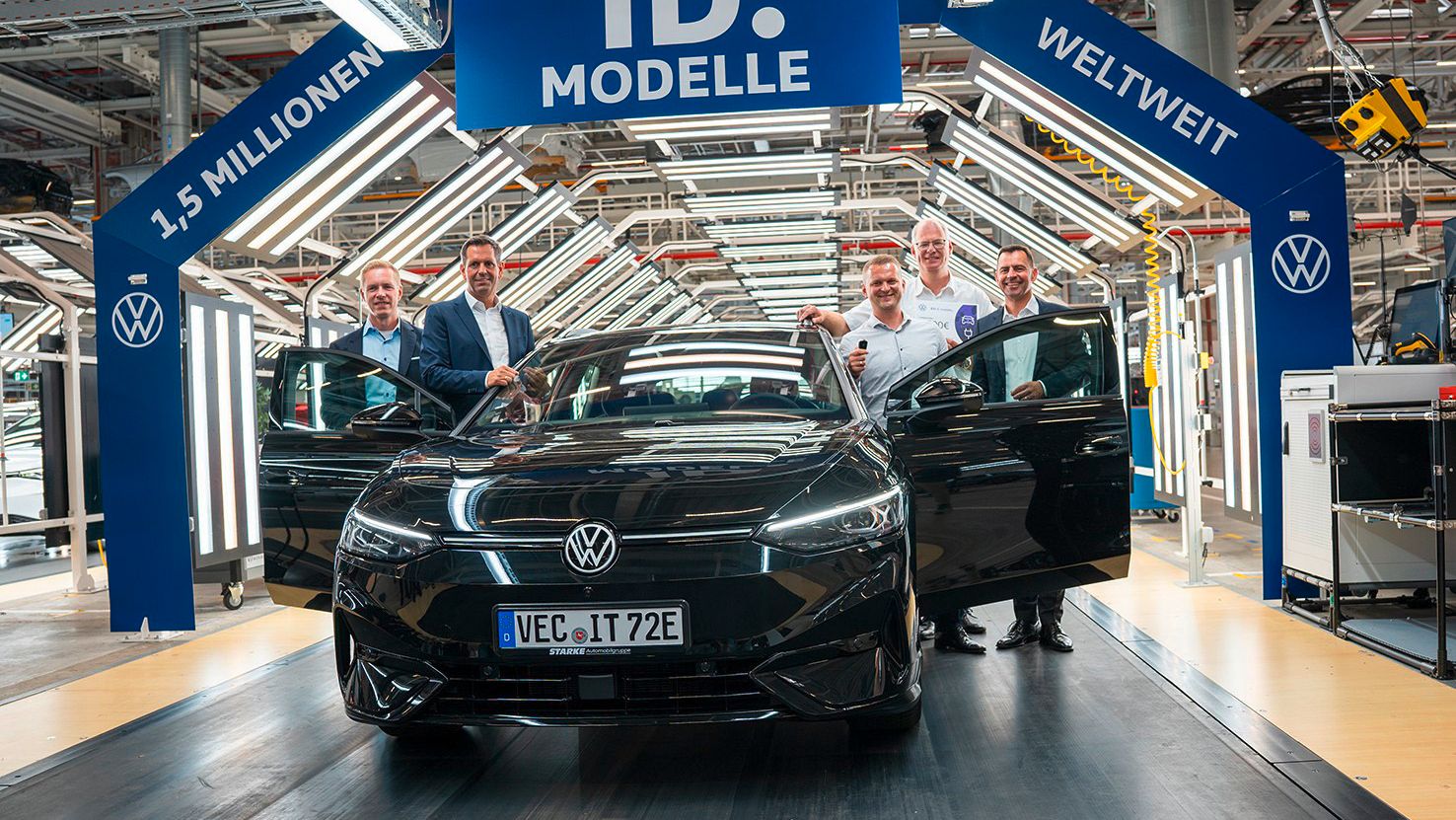 Automobil v továrni obklopený piatimi mužmi. Nad automobilom je veľký modrý banner s nápisom "1,5 Milionen ID. Modelle weltweit". V pozadí vidieť výrobné zariadenia.