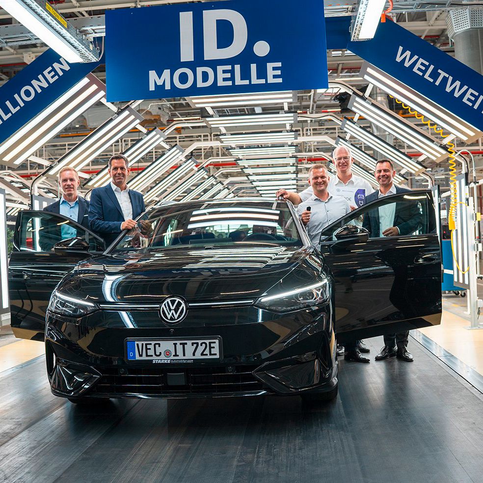 Automobil v továrni obklopený piatimi mužmi. Nad automobilom je veľký modrý banner s nápisom "1,5 Milionen ID. Modelle weltweit". V pozadí vidieť výrobné zariadenia.