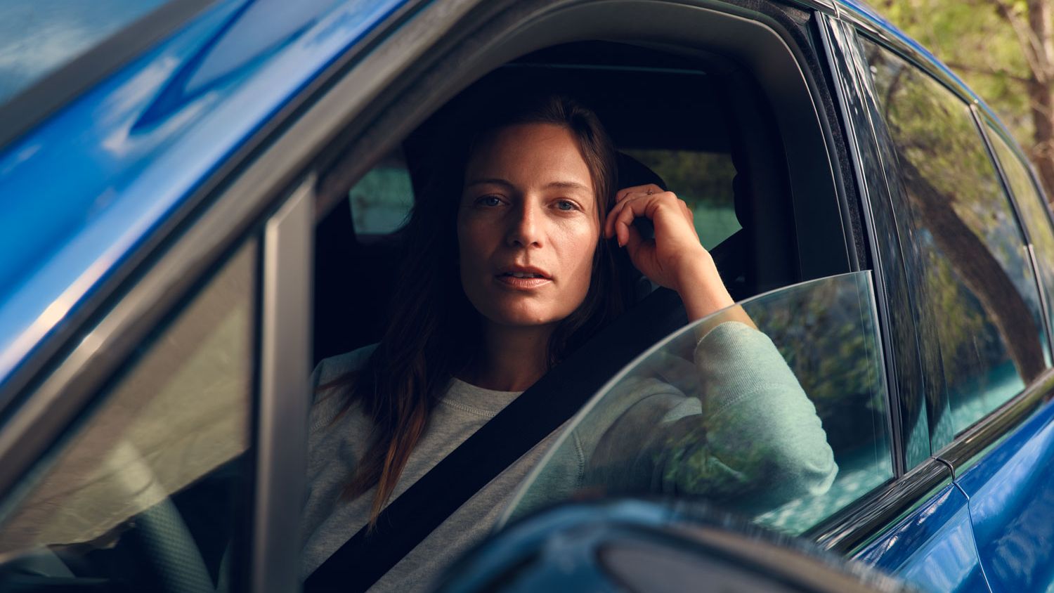 Žena sedí vo vozidle VW Touareg R eHybrid a cez stiahnuté bočné okno sa pozerá priamo do kamery. Za vozidlom je vidieť stromy.