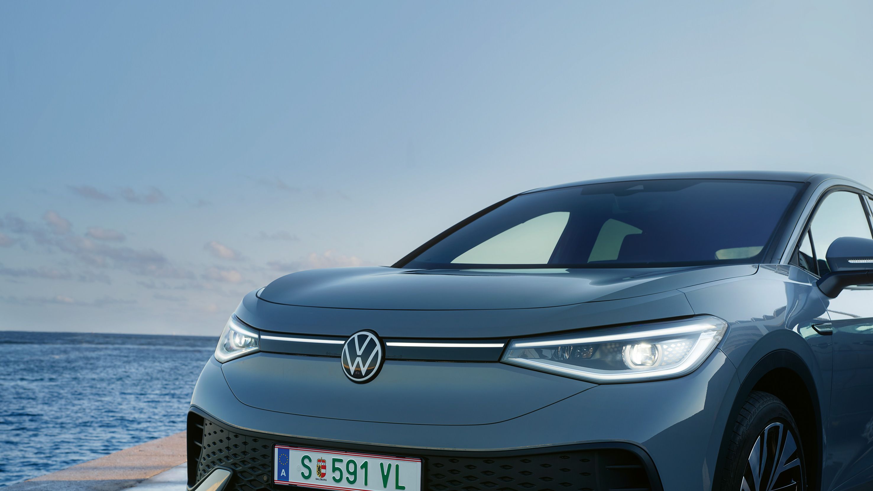Volkswagen ID.5 zaparkovaný na móle pri mori. Auto má moderný dizajn s úzkymi prednými svetlami.