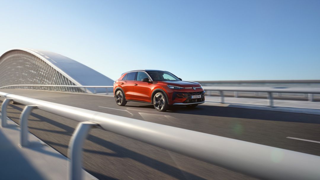 Červený VW T-Roc Style prechádza po modernom moste s nosnú konštrukciu v tvare oblúka.