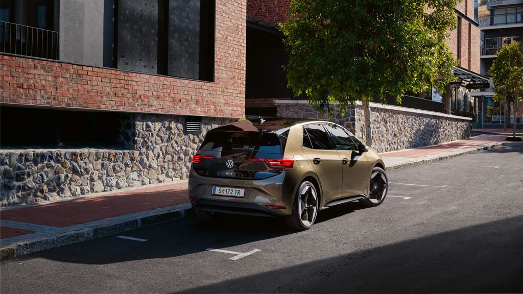 Pohľad na VW ID.3 IQ. LIGHT LED zadné svetlá zozadu. Vozidlo stojí na parkovacom mieste pri modernej bytovej budove s tehlovou fasádou.