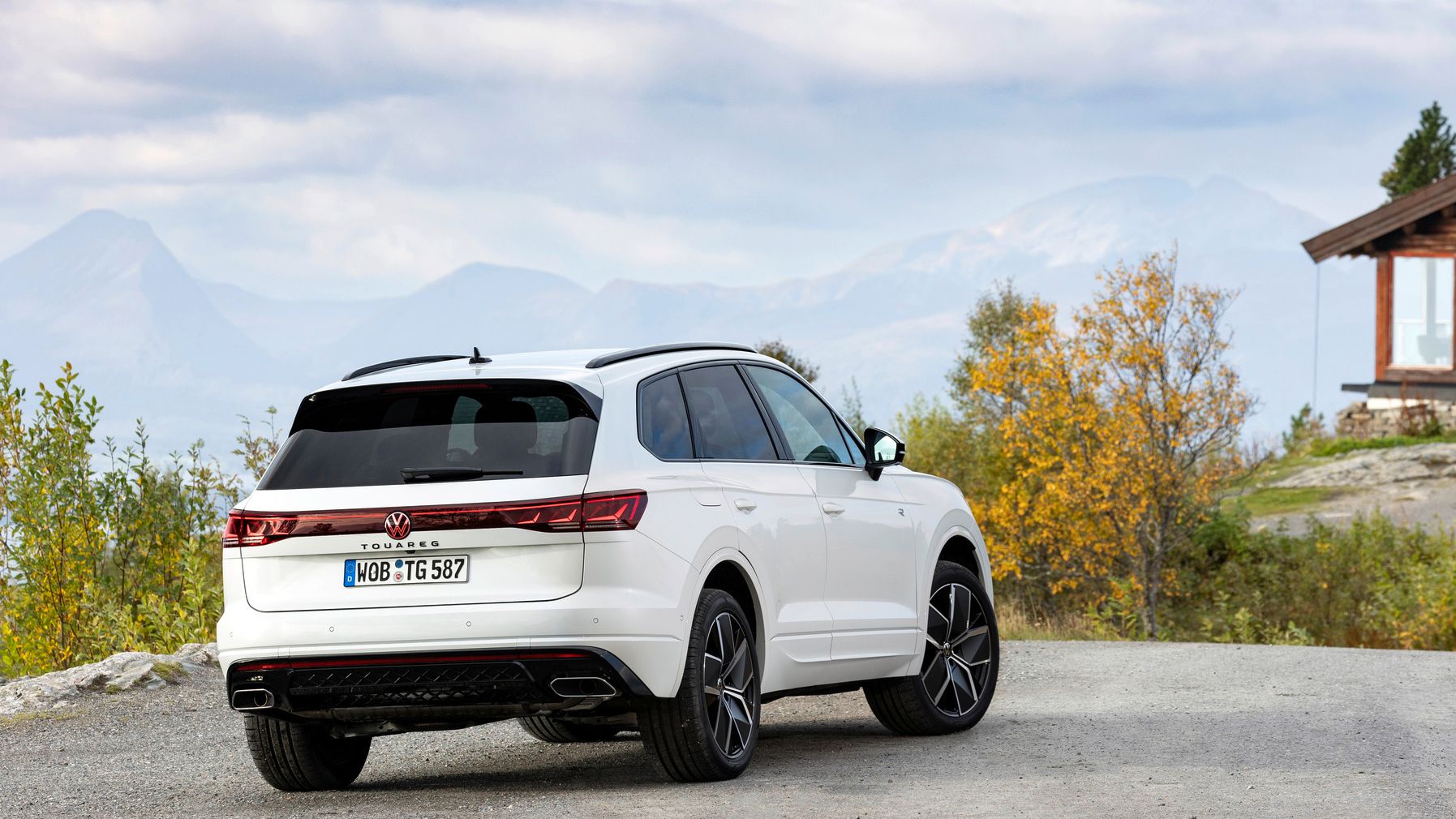 Biely Volkswagen Touareg zaparkovaný na štrkovom odpočívadle  v prírode. V pozadí vidieť dom a hory.