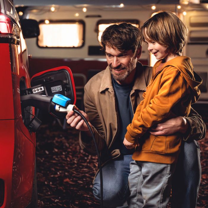 Otec a dieťa využívajú ID. ako zdroj elektrickej energie, v pozadí je v noci osvetlený karavan so svetlenou reťazou.