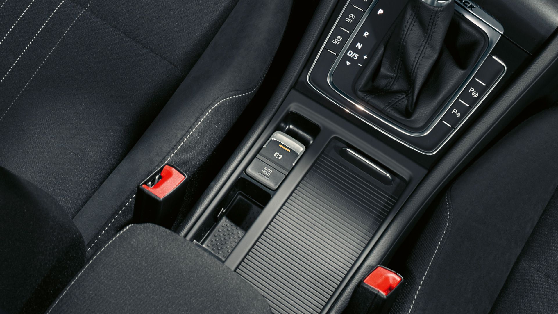Detailný pohľad na stredovú konzolu automobilu s automatickou prevodovkou. Vidieť čiernu radiacu páku a stredový panel s rôznymi tlačidlami. Na obrázku sú tiež nápadné červené časti bezpečnostných klipov.