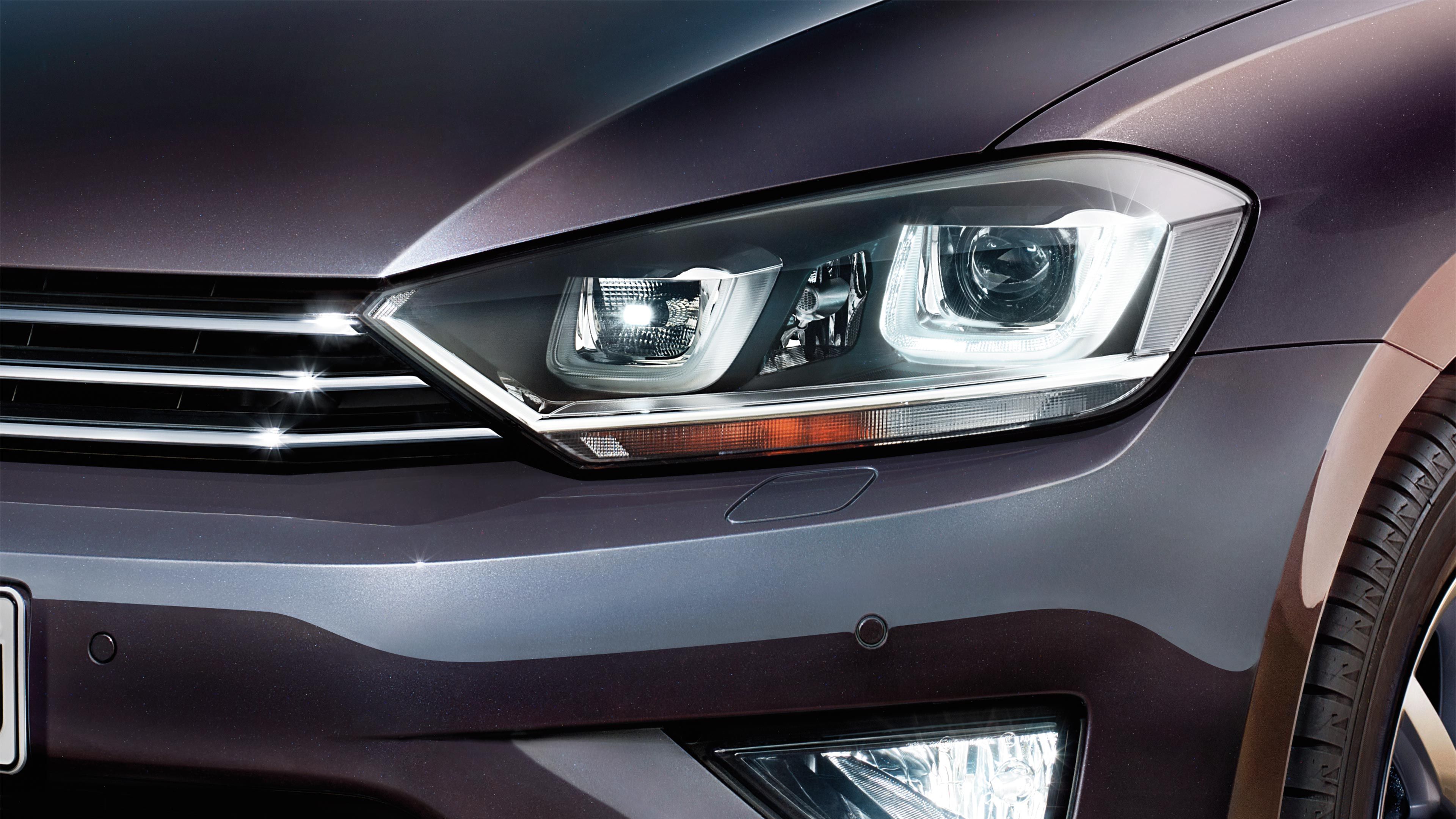 Detailný pohľad na predný svetlomet moderného automobilu. Svetlomet je vo vypnutom stave a automobil má tmavo sivú farbu. Na obrázku je vidieť aj časť predného nárazníka a kapoty.
