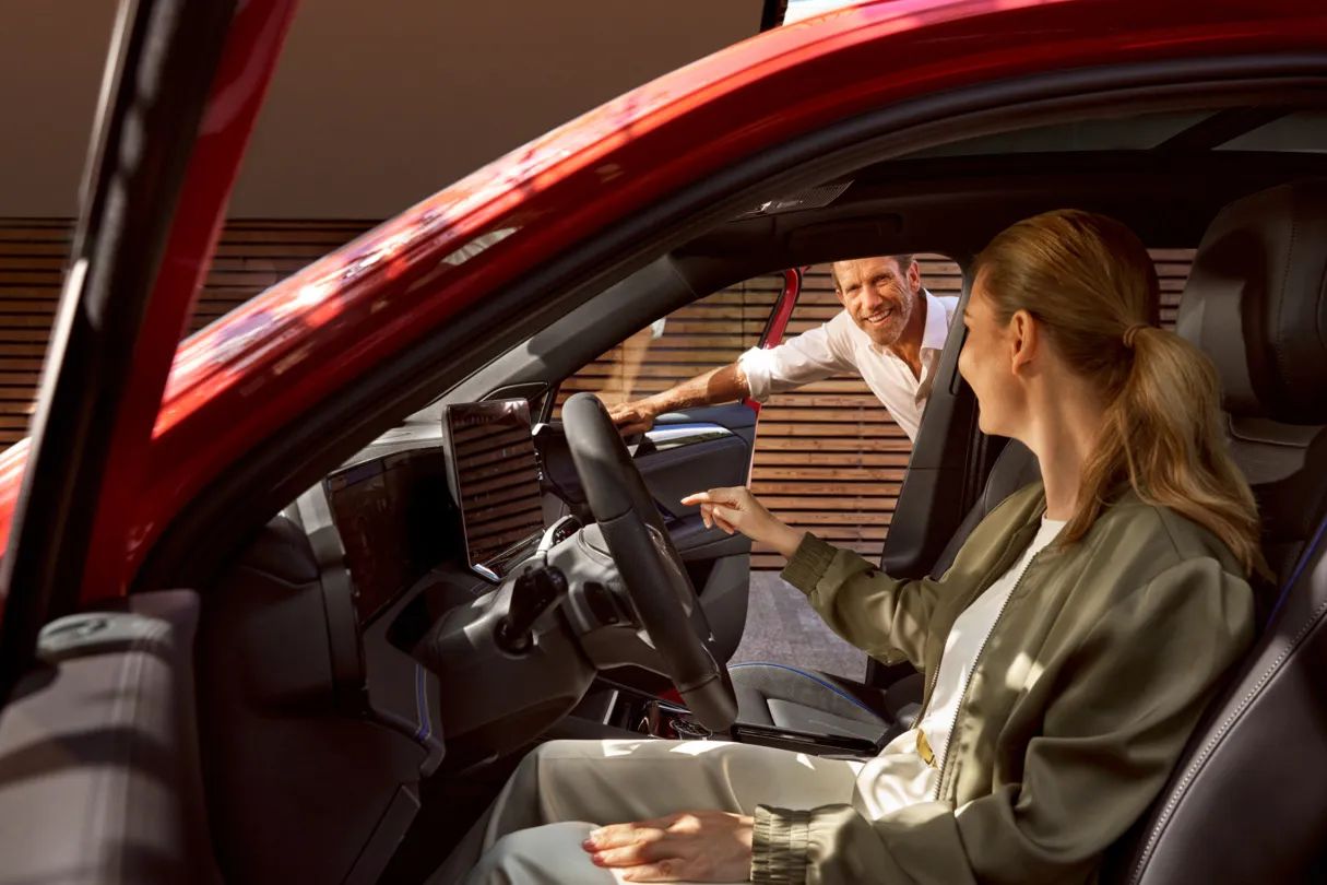 Žena sedí vo vozidle Volkswagen, muž sa pozerá dnu cez otvorené dvere spolujazdca a spolu o ničom diskutujú.