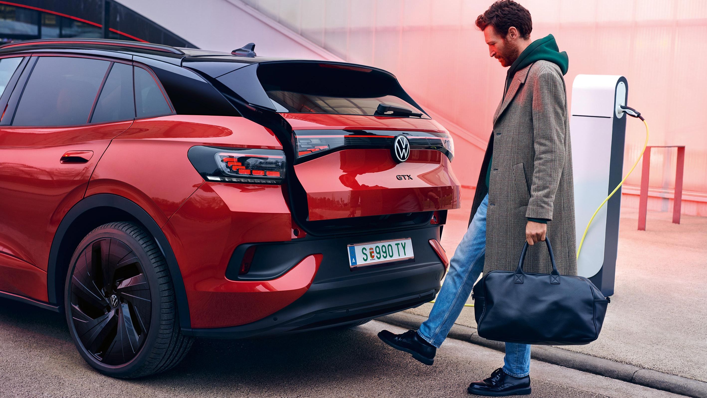 VW ID.4 GTX v červenej farbe pri pohľade zozadu, muž s taškou otvára dvere batožinového priestoru prostredníctvom nohy pod zadným nárazníkom.