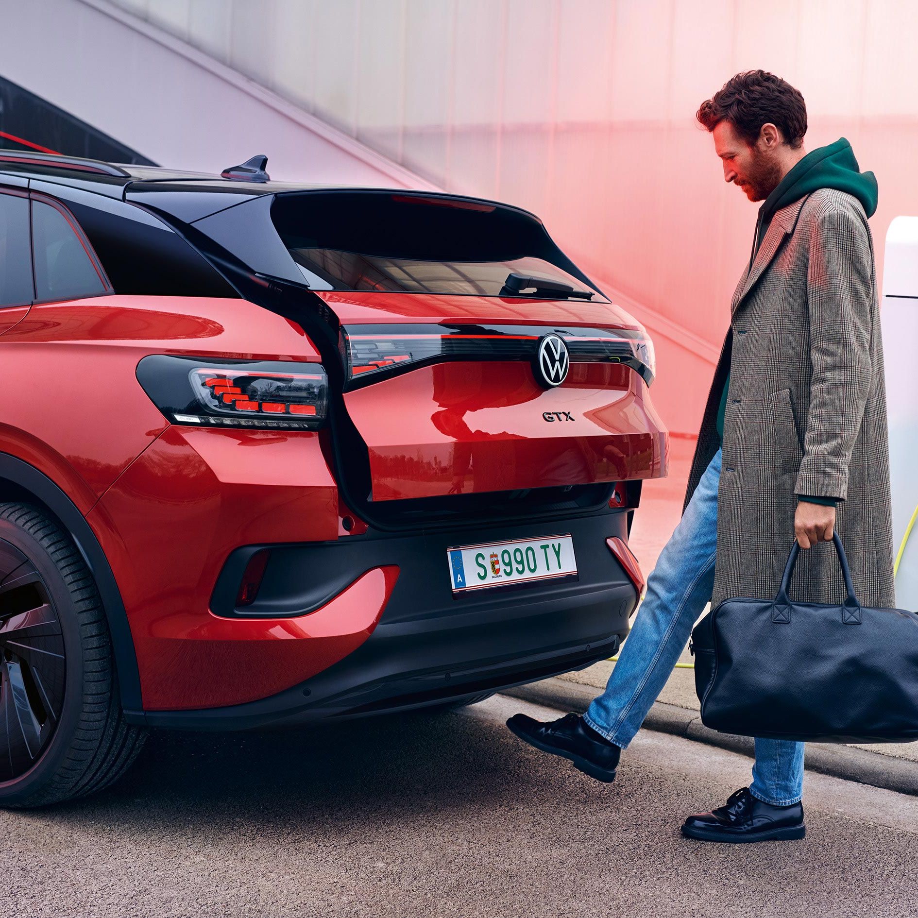 VW ID.4 GTX v červenej farbe pri pohľade zozadu, muž s taškou otvára dvere batožinového priestoru prostredníctvom nohy pod zadným nárazníkom.