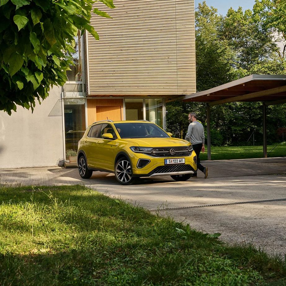 Muž sa chystá nastúpiť do žltého VW T-Cross, ktoré je zaparkované na príjazdovej ceste k domu.