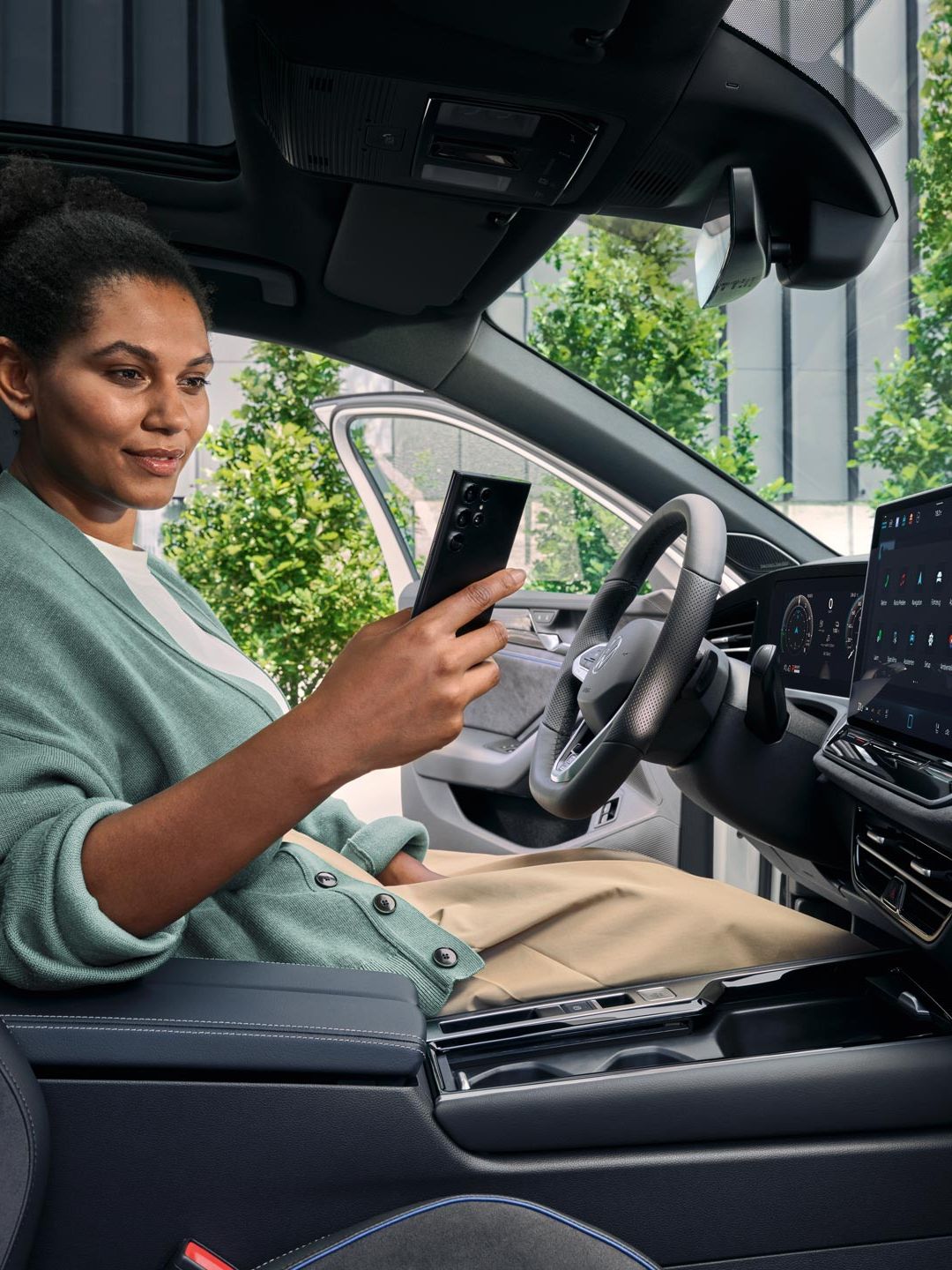 Žena sedí na mieste vodiča zaparkovaného VW Passat s otvorenými dverami a pozerá na svoj smartfón.