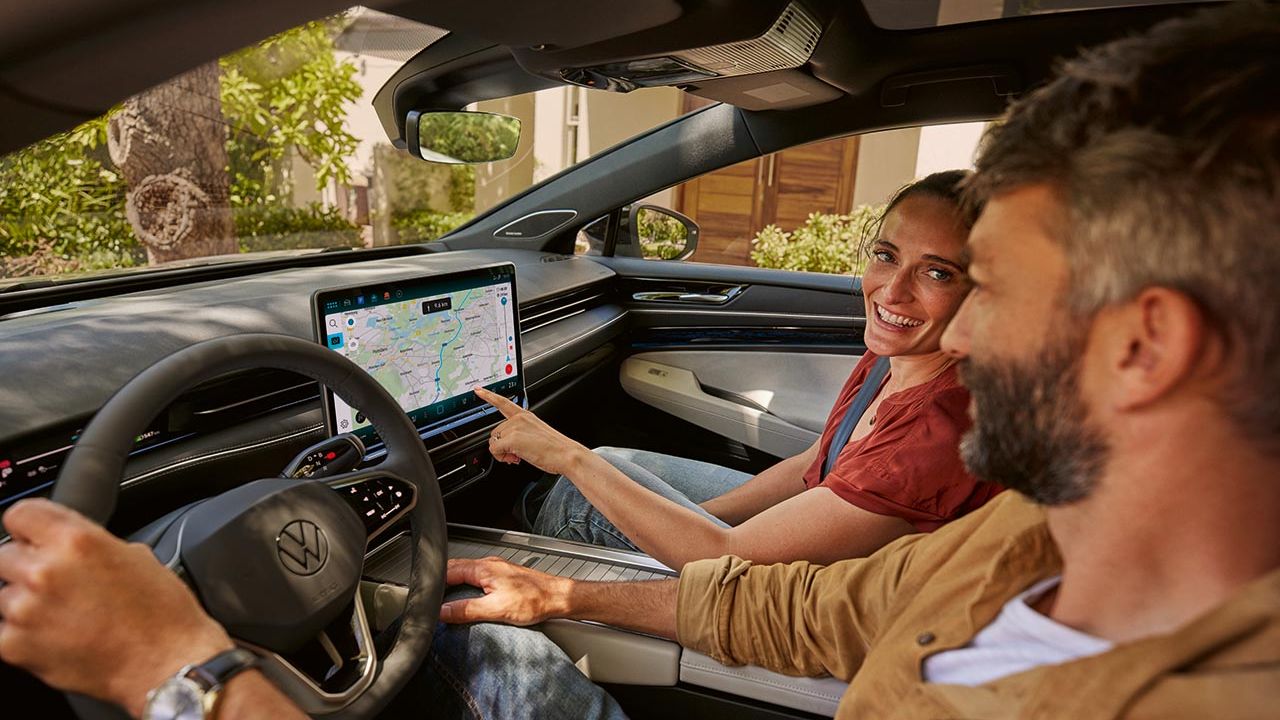 V prednej časti vozidla VW ID.7 sedia muž a žena; žena ukazuje na mapu v systéme infotainment.