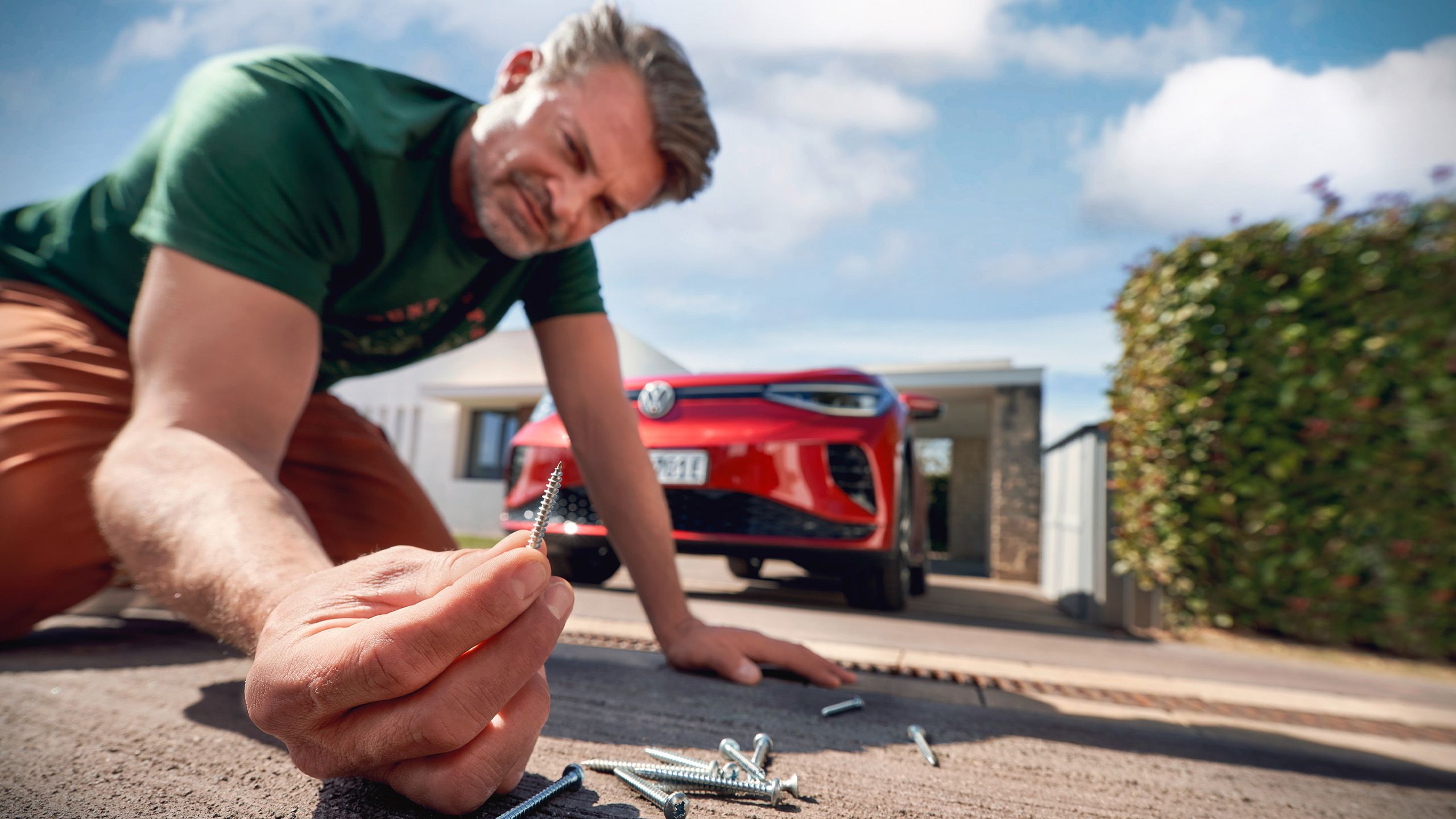 Muž kontroluje skrutky, ktoré ležia v príjazdovej ceste, v pozadí VW ID.5 GTX