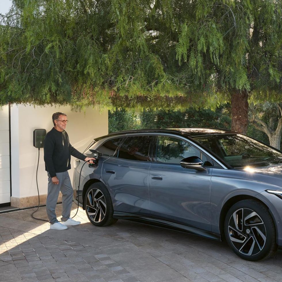 Muž stojí vedľa modrého VW ID.7 Tourer, ktorý sa nabíja pred garážou pri nabíjacej stanici Wallbox.