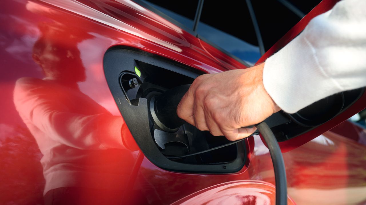 Nejaká osoba zapája nabíjací kábel do vozidla VW.