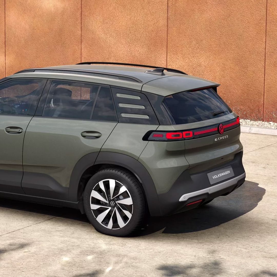 Olivovo zelený VW ID. Cross Style stojí na betónovej ploche pred hrdzavou stenou. Vozidlo má čierne strešné nosiče, tónované okná a charakteristické LED zadné svetlá s niekoľkými horizontálnymi pruhmi. Disky sú dvojfarebné v čiernej a striebornej farbe.
