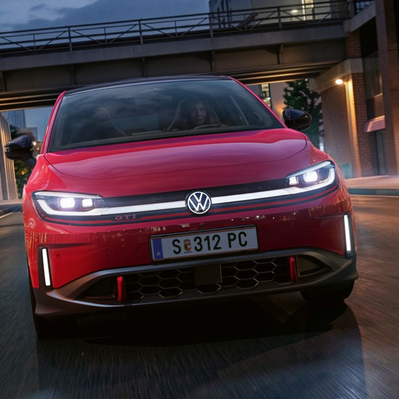 Jedna osoba riadi červené VW ID. Polo GTI modernou osvetlenou obchodnou štvrťou večer.