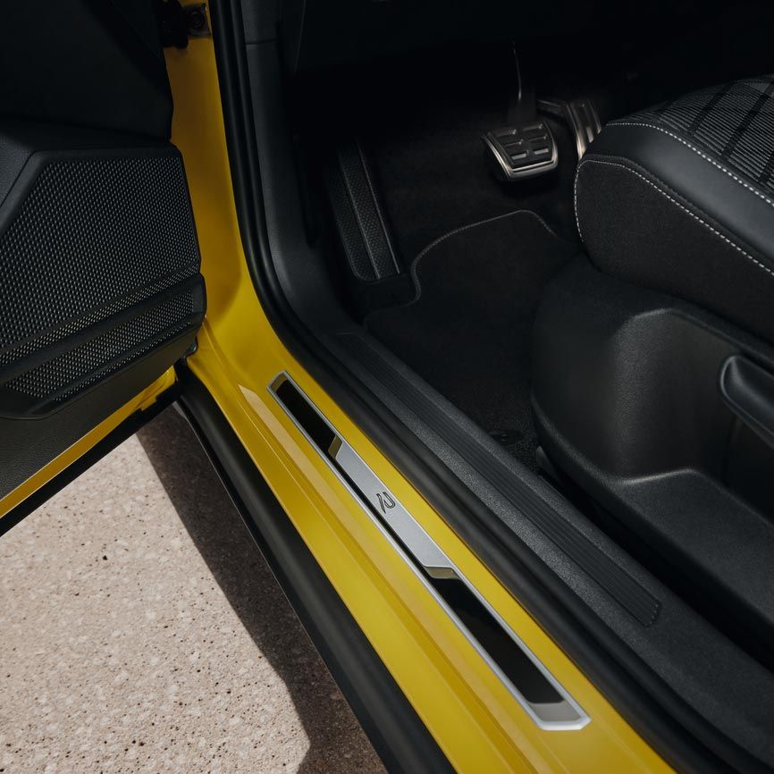 Pohľad na spodnú časť sedadla vodiča žltého VW T-Cross s otvorenými prednými dverami s prahovou lištou z brúsenej ušľachtilej ocele.