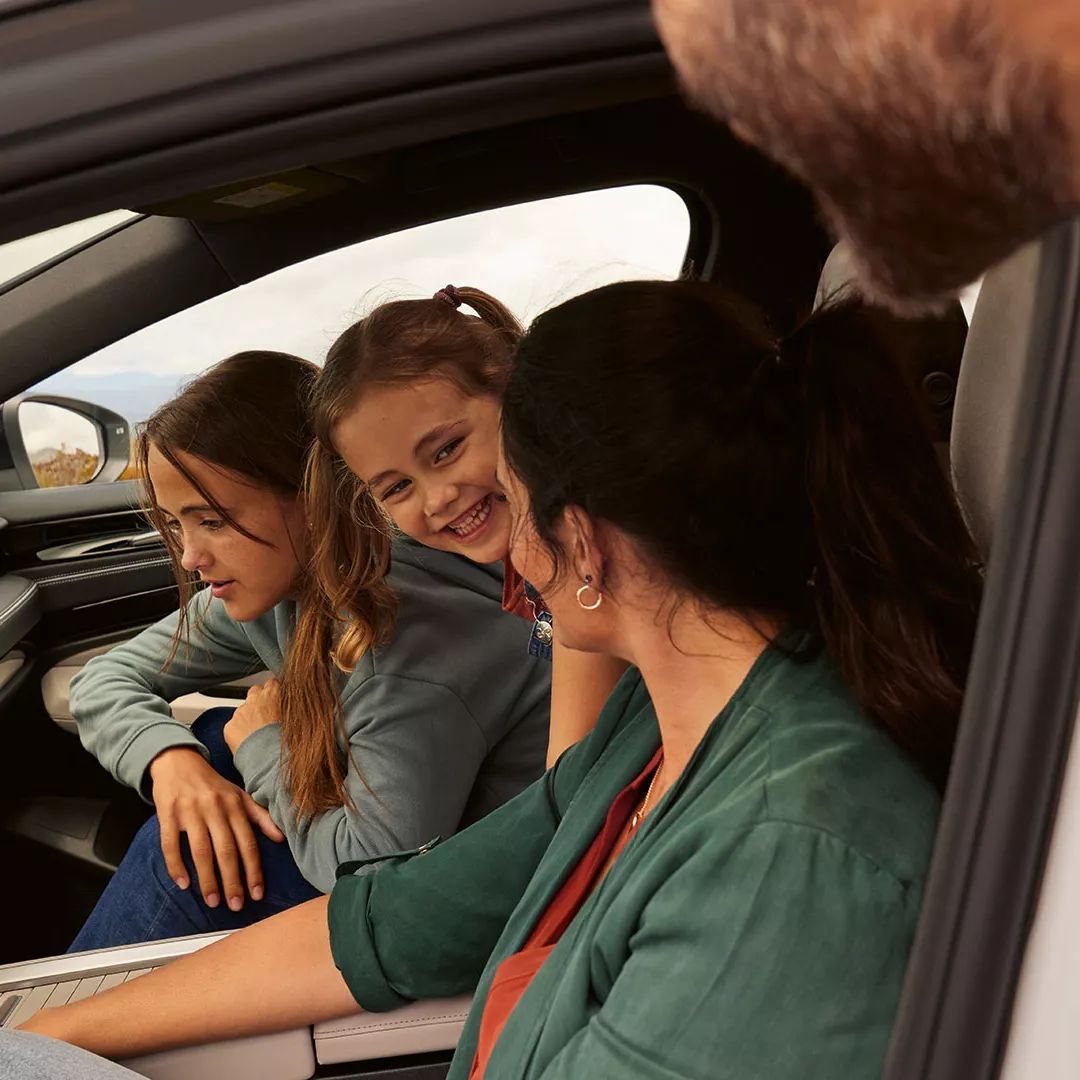 Dve deti a žena sa pozerajú na systém Infotainment vo vozidle Volkswagen ID.7. Otec sa pozerá cez dvere vodiča.