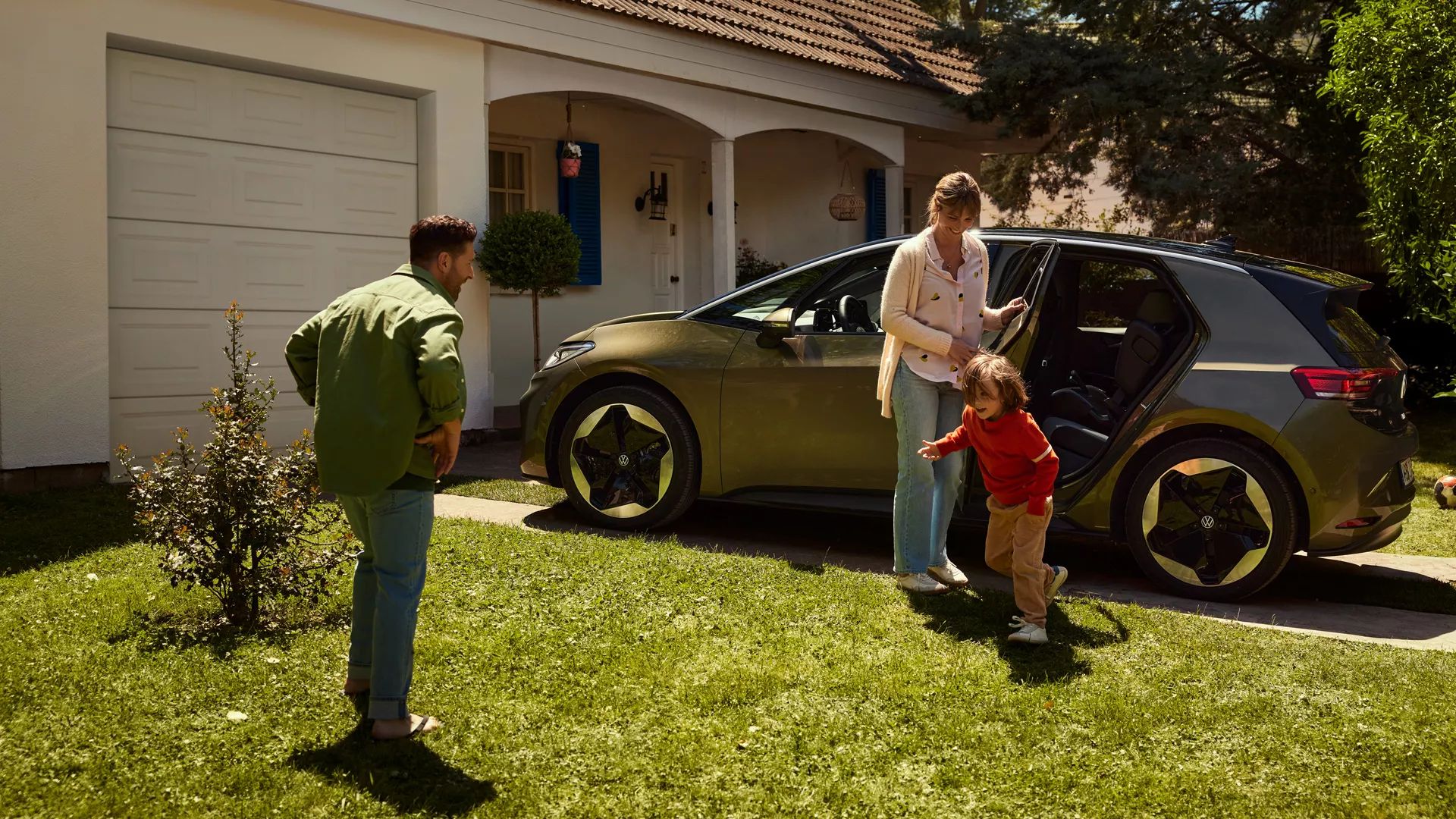Pred obytným domom stojí ID.3. Matka otvára zadné dvere, zatiaľ čo dieťa beží k otcovi na trávniku.