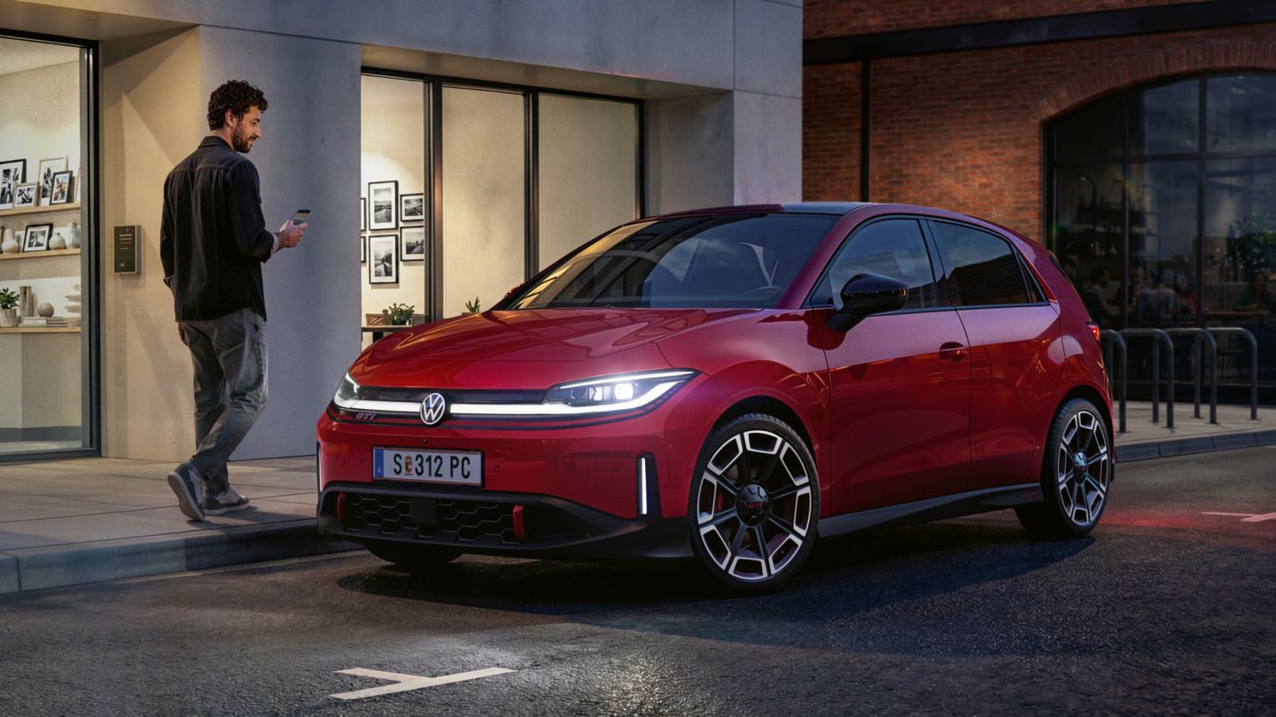 Človek prechádza okolo červeného VW ID. Polo GTI, ktoré parkuje pred modernou budovou.