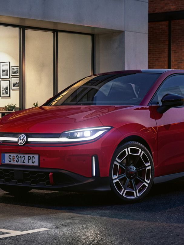 Človek prechádza okolo červeného VW ID. Polo GTI, ktoré parkuje pred modernou budovou.