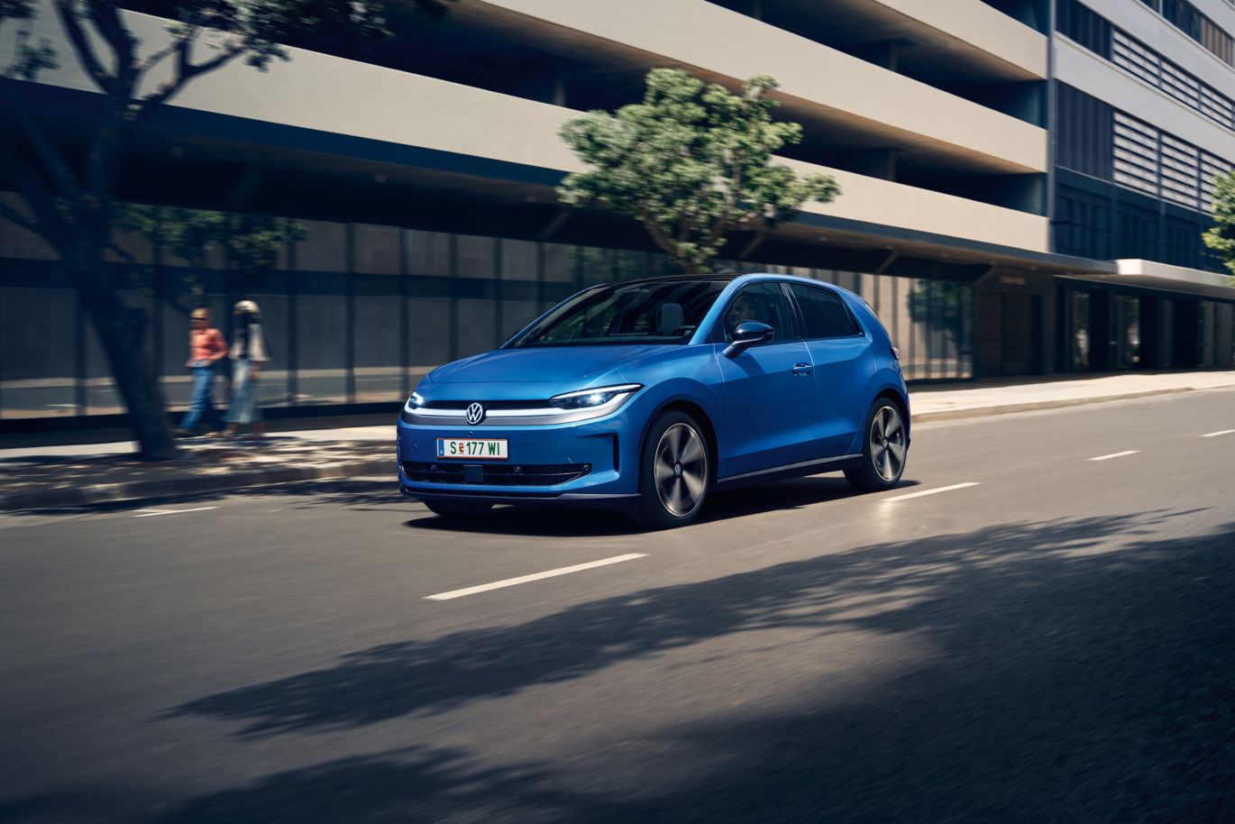 Modrý VW ID. Polo Style prechádza mestom so zelenými stromami pozdĺž cesty.