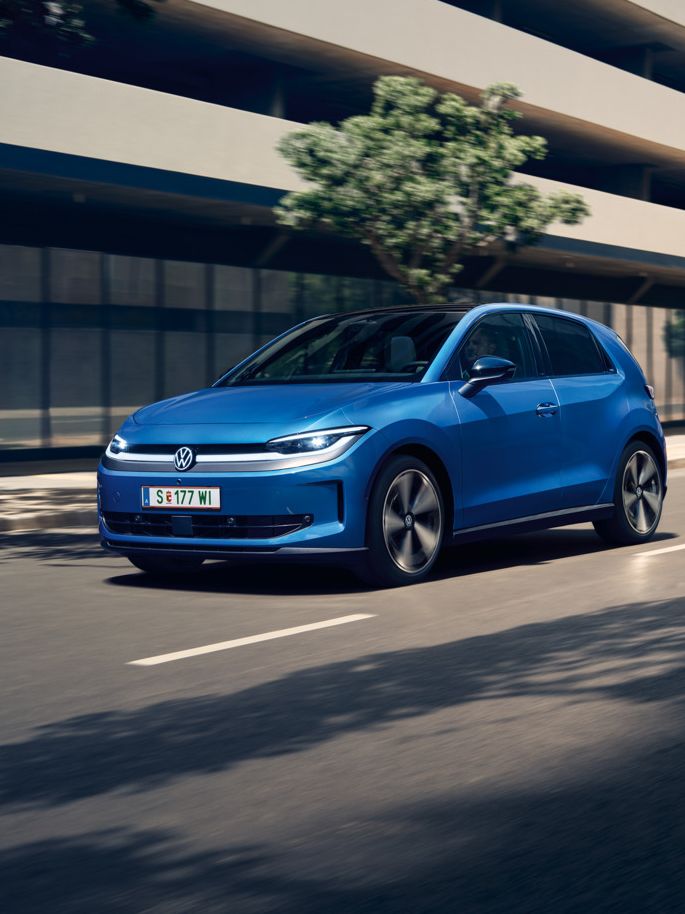 Modrý VW ID. Polo Style prechádza mestom so zelenými stromami pozdĺž cesty.