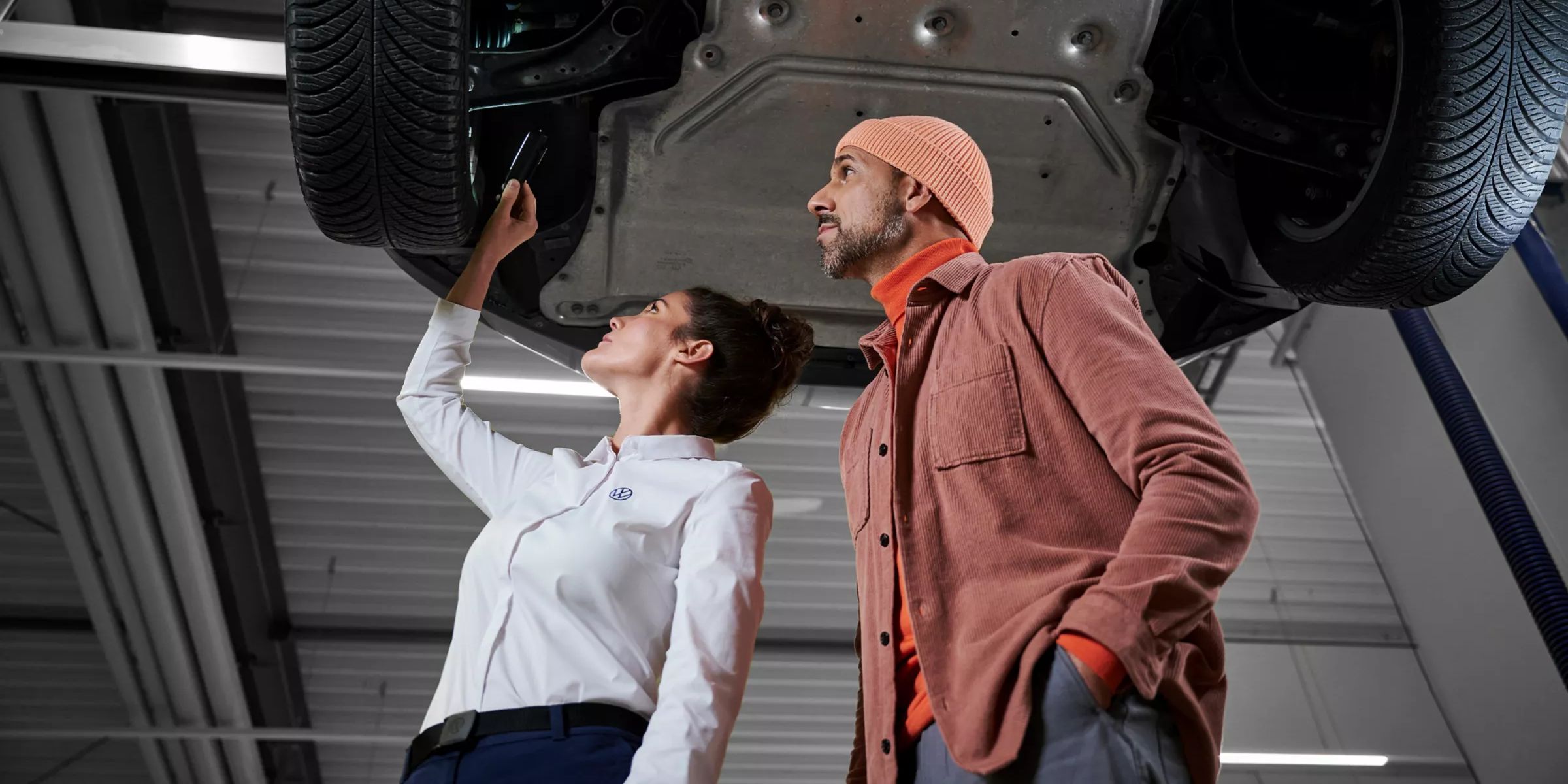 Servisná pracovníčka VW a zákazník kontrolujú podvozok vozidla VW – náhradné diely VW