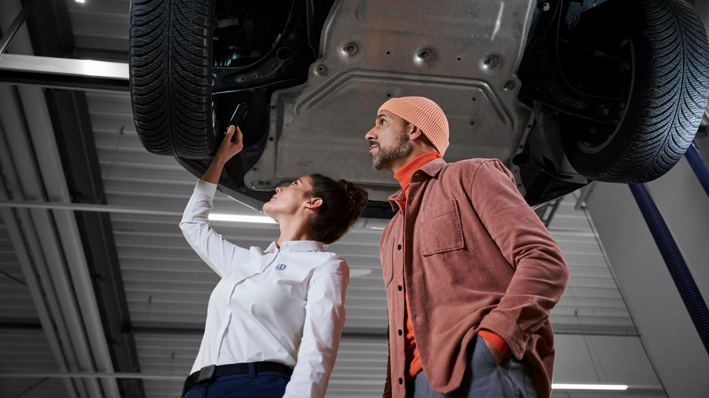 Servisná pracovníčka VW a zákazník kontrolujú podvozok vozidla VW – náhradné diely VW
