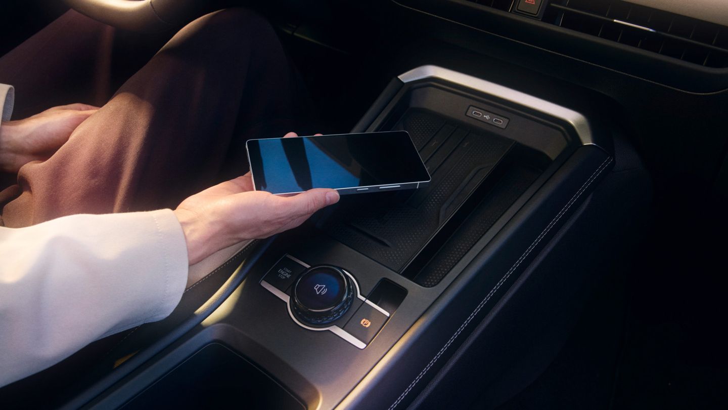 Osoba drží smartfón a položí ho na bezdrôtovú nabíjacú plochu vo vnútri auta. Pozornosť je upriamená na stredovú konzolu vozidla.