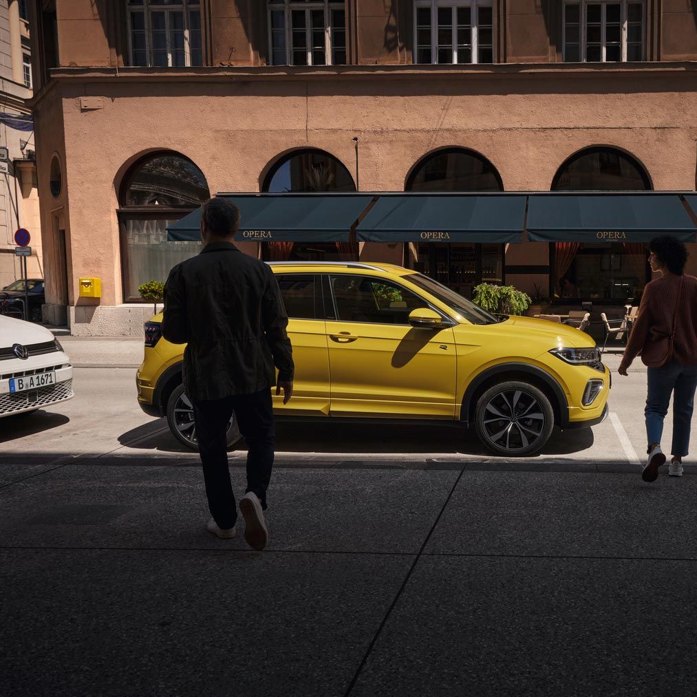 Muž a žena sa približujú k žltému VW T-Cross na okraji cesty.