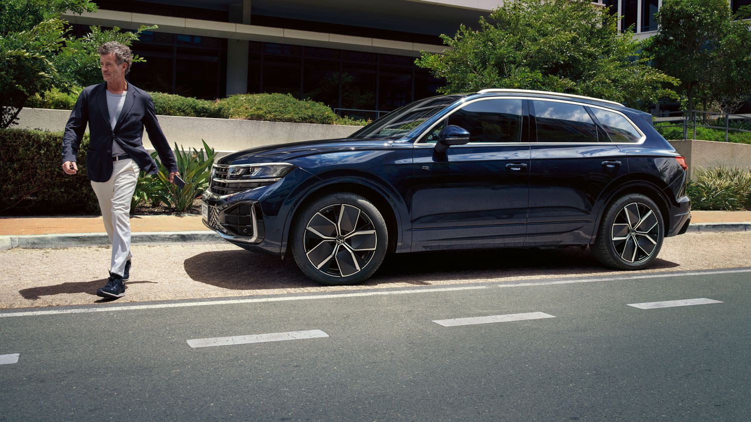 Muž prechádza cez cestu pred zaparkovaným vozidlom VW Touareg.