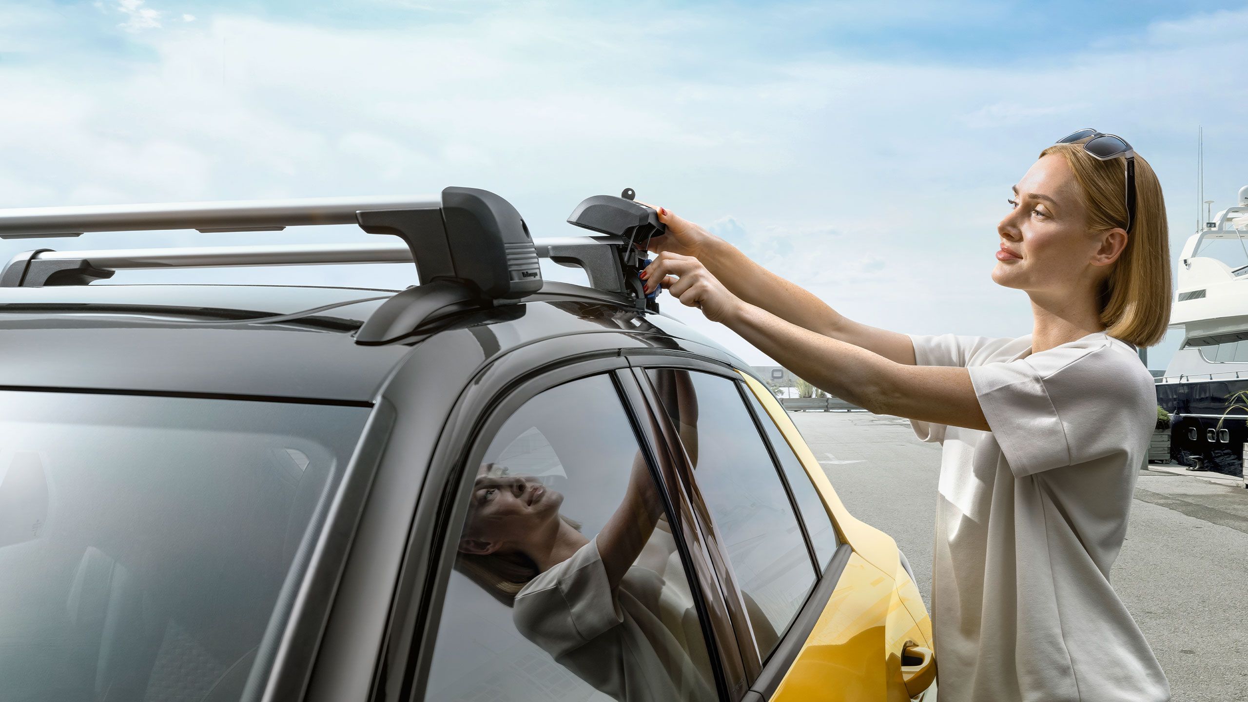 Žena pripevňuje priečne nosníky z príslušenstva VW na strechu nového vozidla VW T-Roc.