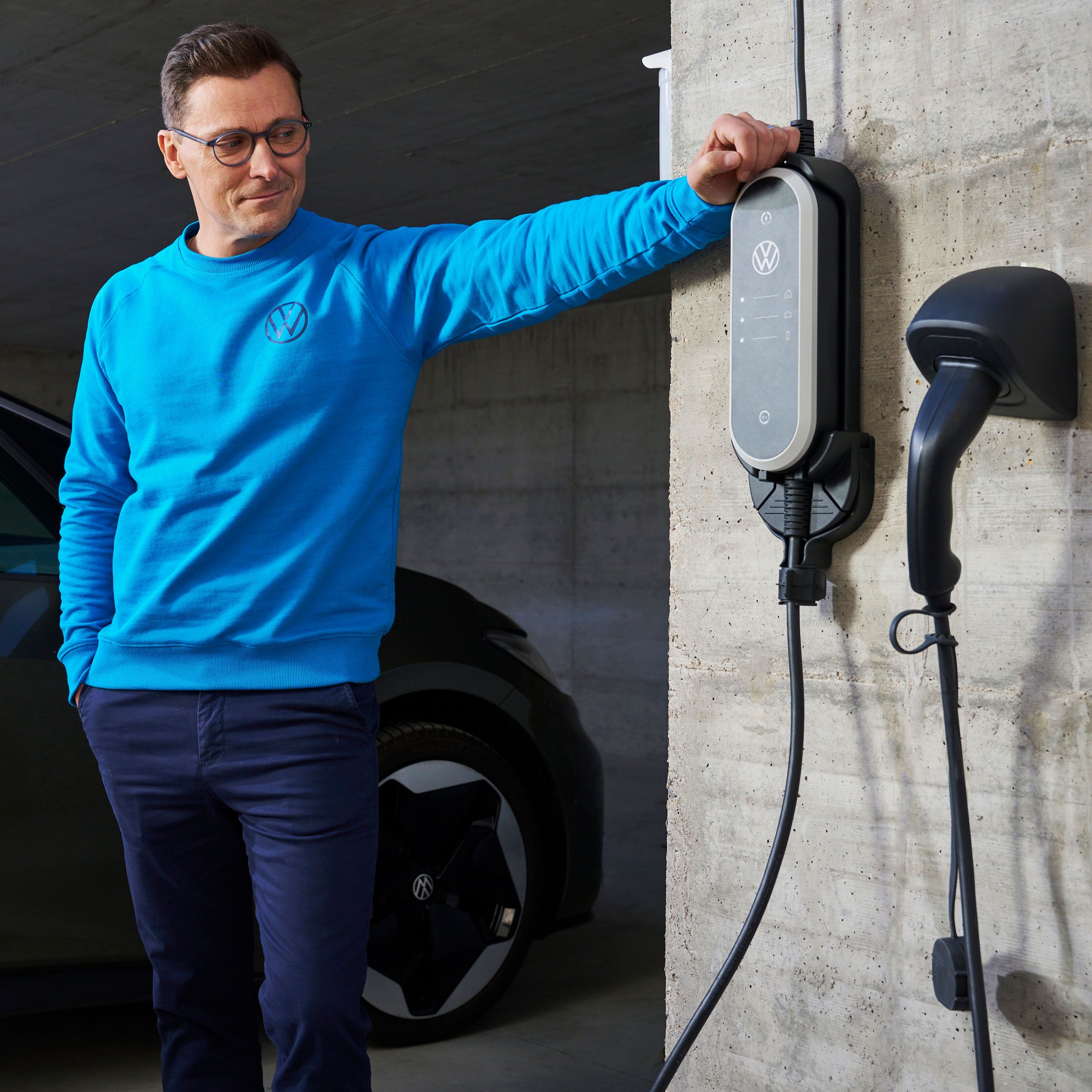 Muž stoji vedľa ID. Charger Travel z príslušenstva Volkswagen, VW ID.3 v pozadí