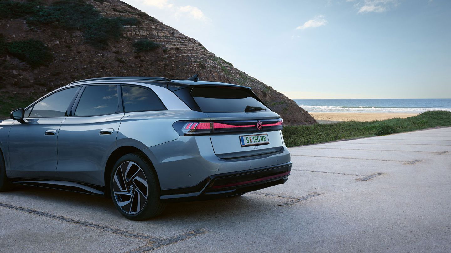 Šedé ID.7 Tourer zaparkované pri morskom pobreží. V pozadí je pláž a more pod modrou oblohou. 