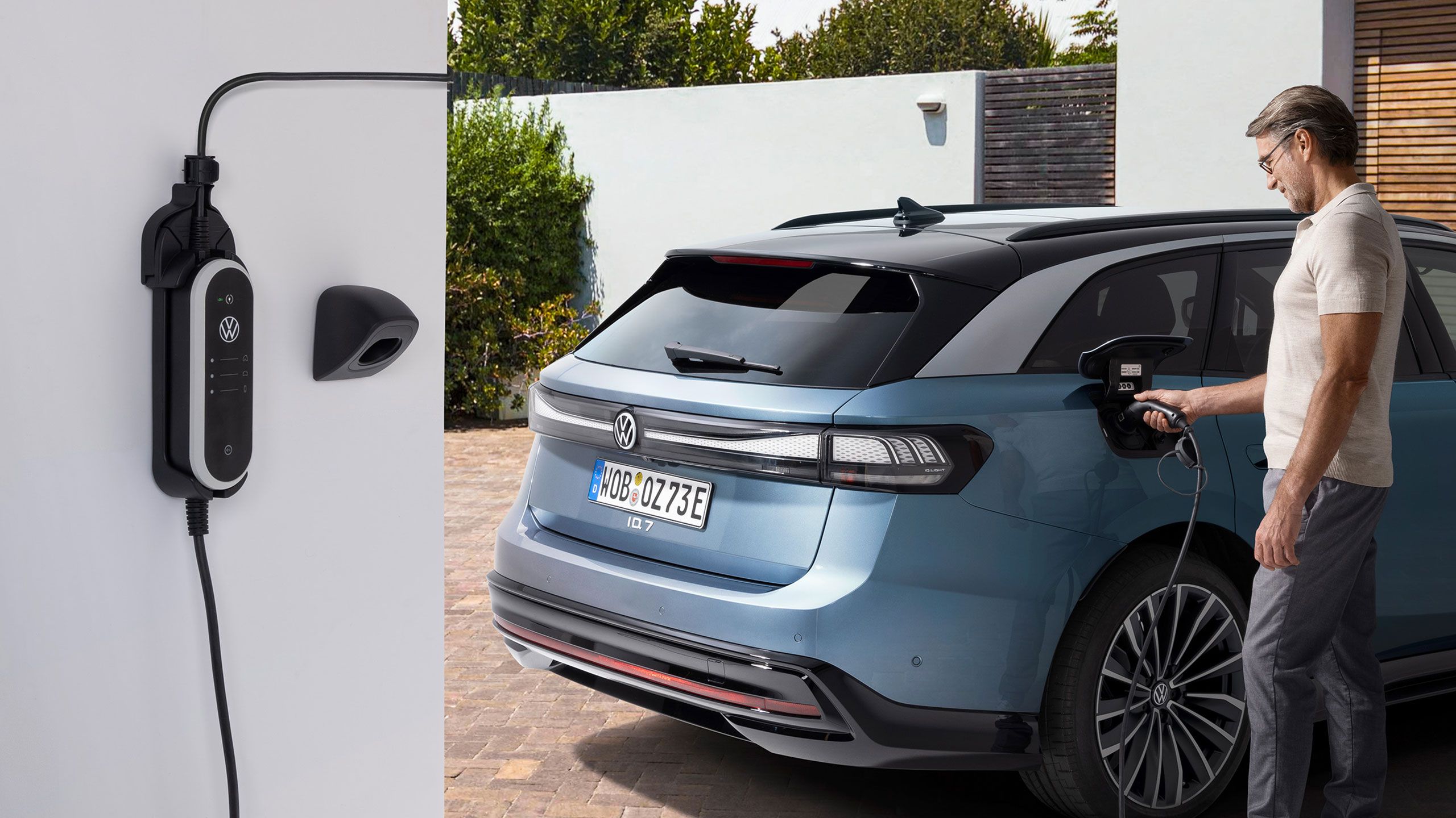 Muž nabíja VW ID.7 Tourer pomocou nabíjacieho kábla – v popredí je sada nabíjacích držiakov na stenu ID. Charger Travel Basis