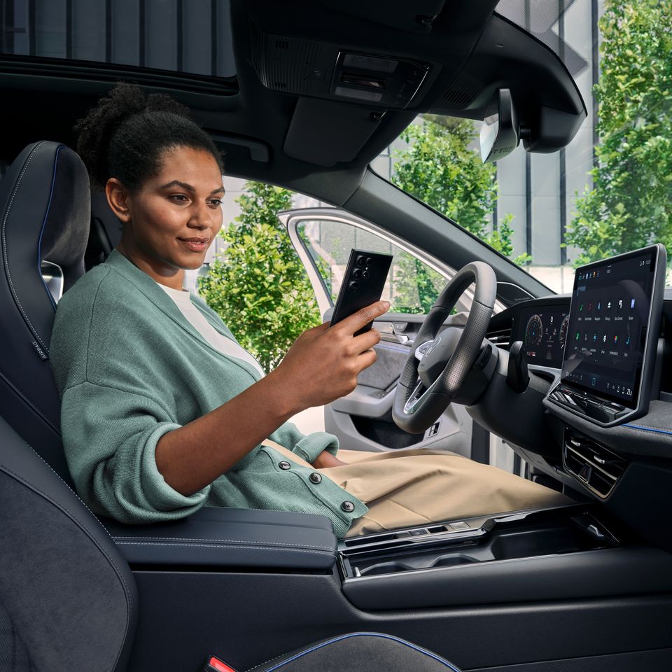 Žena sedí vo vozidle Volkswagen a pozerá sa na mobilný telefón.
