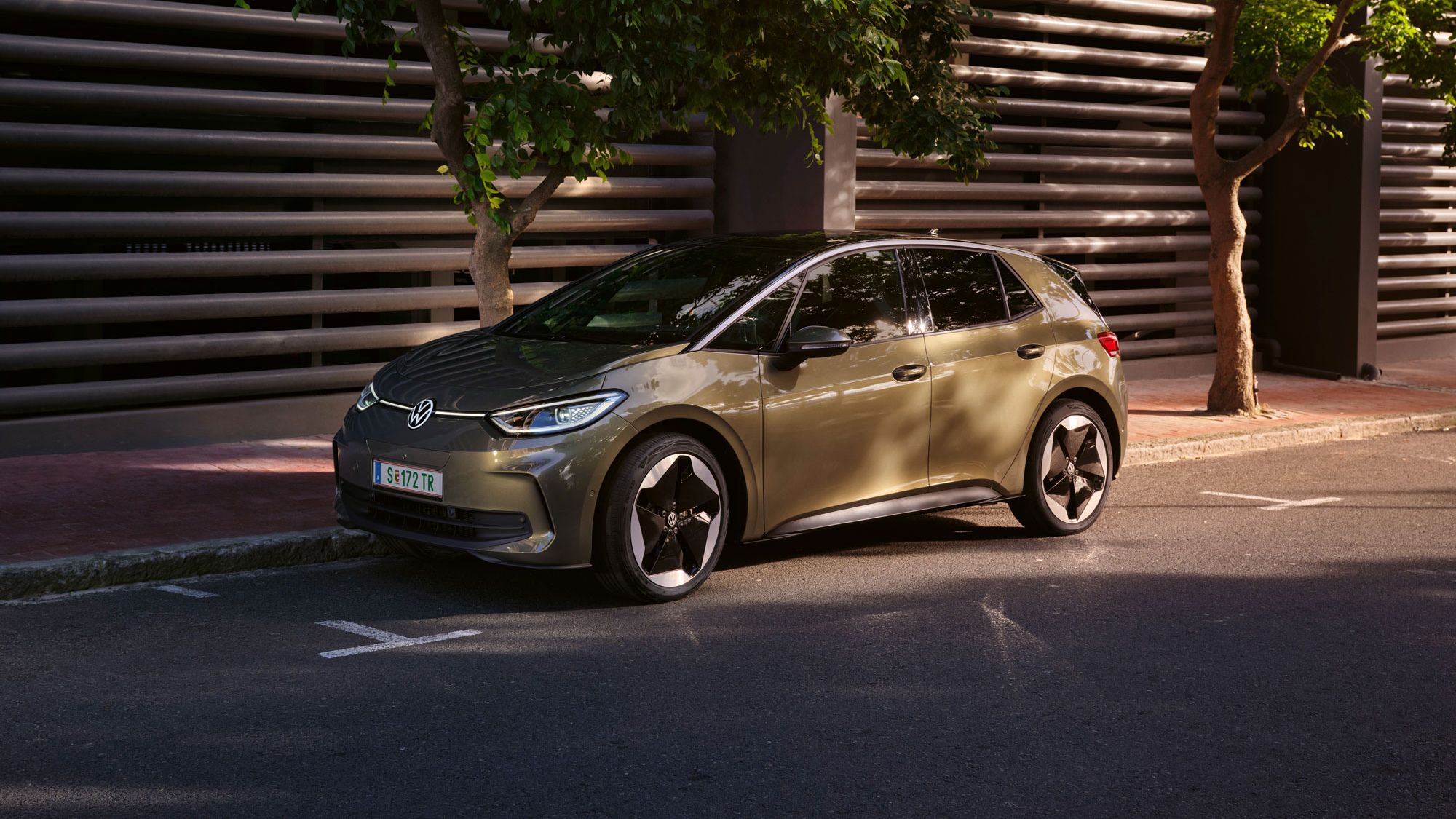 VW ID.3 v olivovo zelenej farbe je zaparkovaný v meste pri modernom bytovom dome.