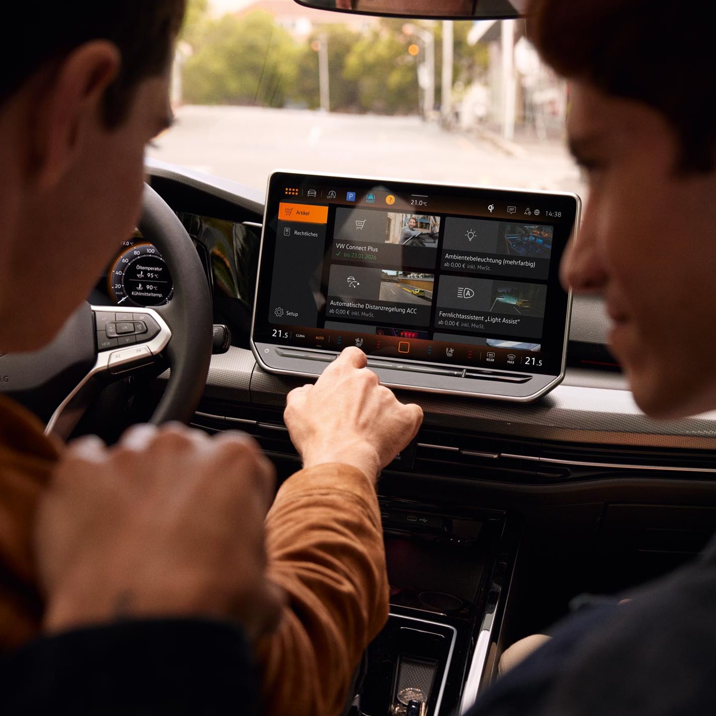 Pohľad do interiéru VW Golf s výhľadom na displej. Muži na sedadle vodiča a spolujazdca ovládajú systém infotainment.