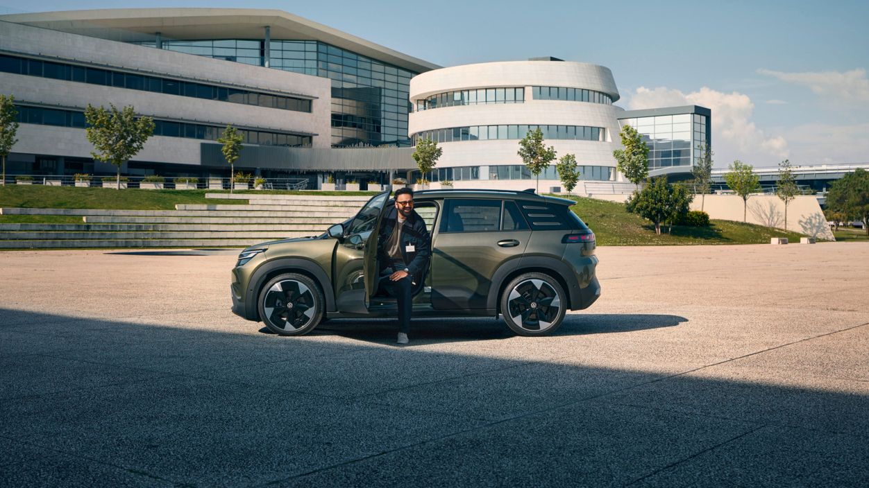 Muž vystupuje z dverí vodiča vozidla VW ID. Cross, ktoré stojí pred modernou viacposchodovou firemnou budovou.