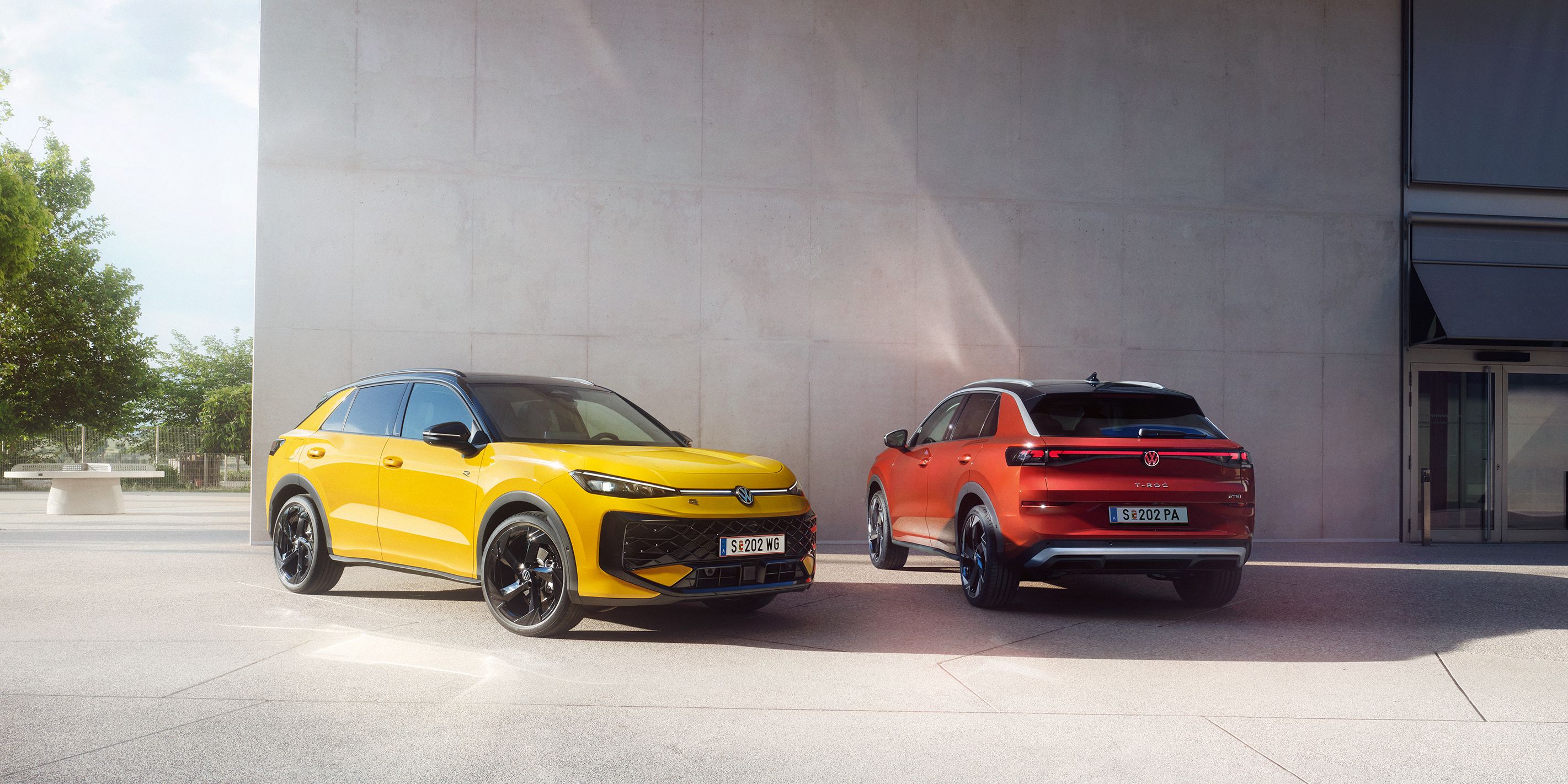 Žltý VW T-Roc R-Line a červený VW T-Roc Style stoja vedľa seba pred modernou budovou.