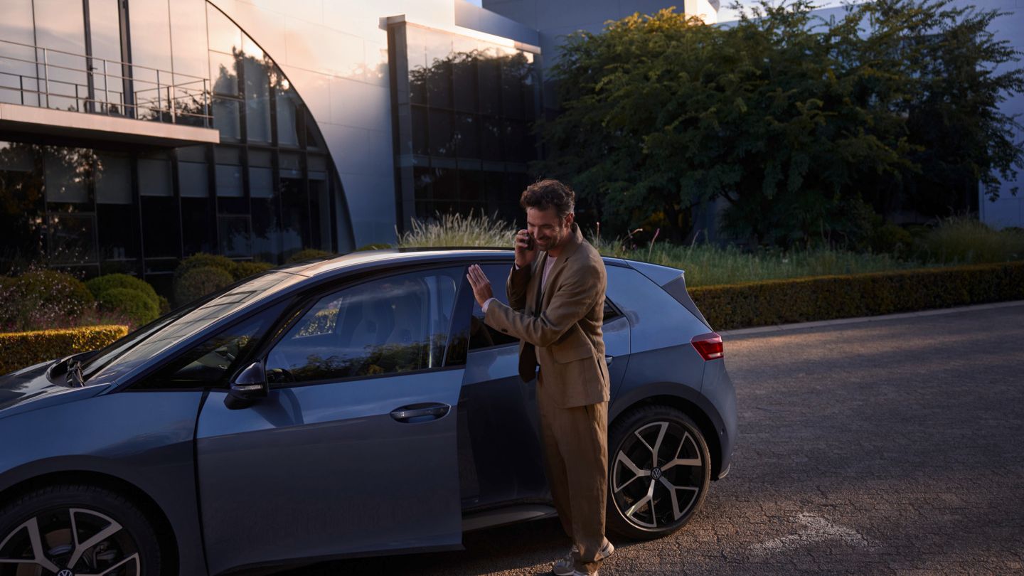 Muž stojí pred modrým vozidlom VW ID.3 Neo a telefonuje cez smartfón.