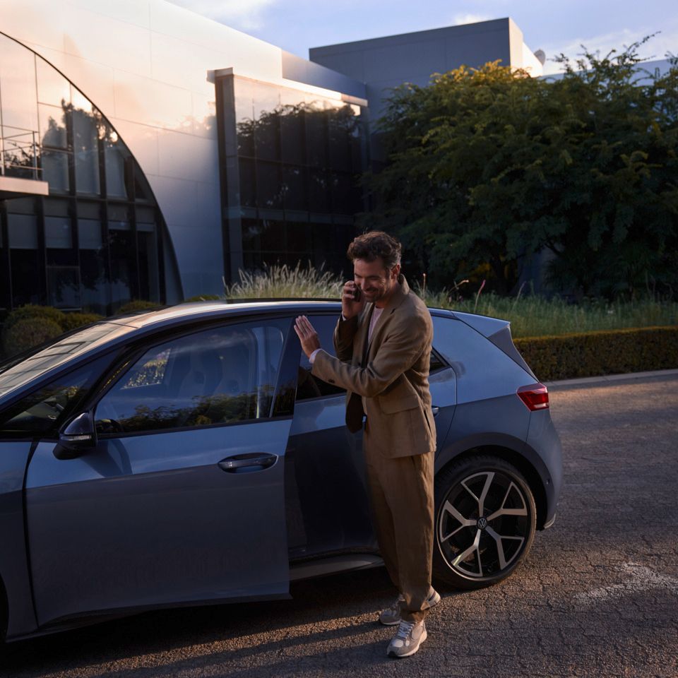 Muž stojí pred modrým vozidlom VW ID.3 Neo a telefonuje cez smartfón.