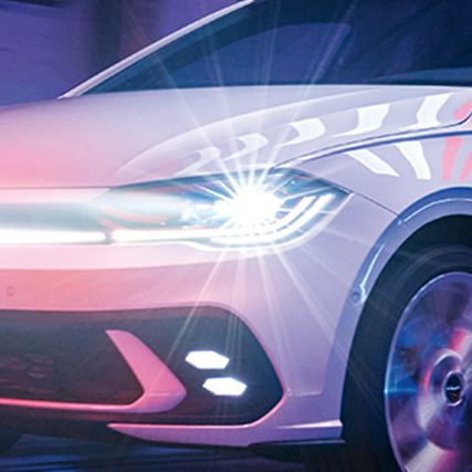 Biely VW Polo GTI jazdí v hale so zapnutými Matrix LED svetlometmi a svetelným pásom vpredu.